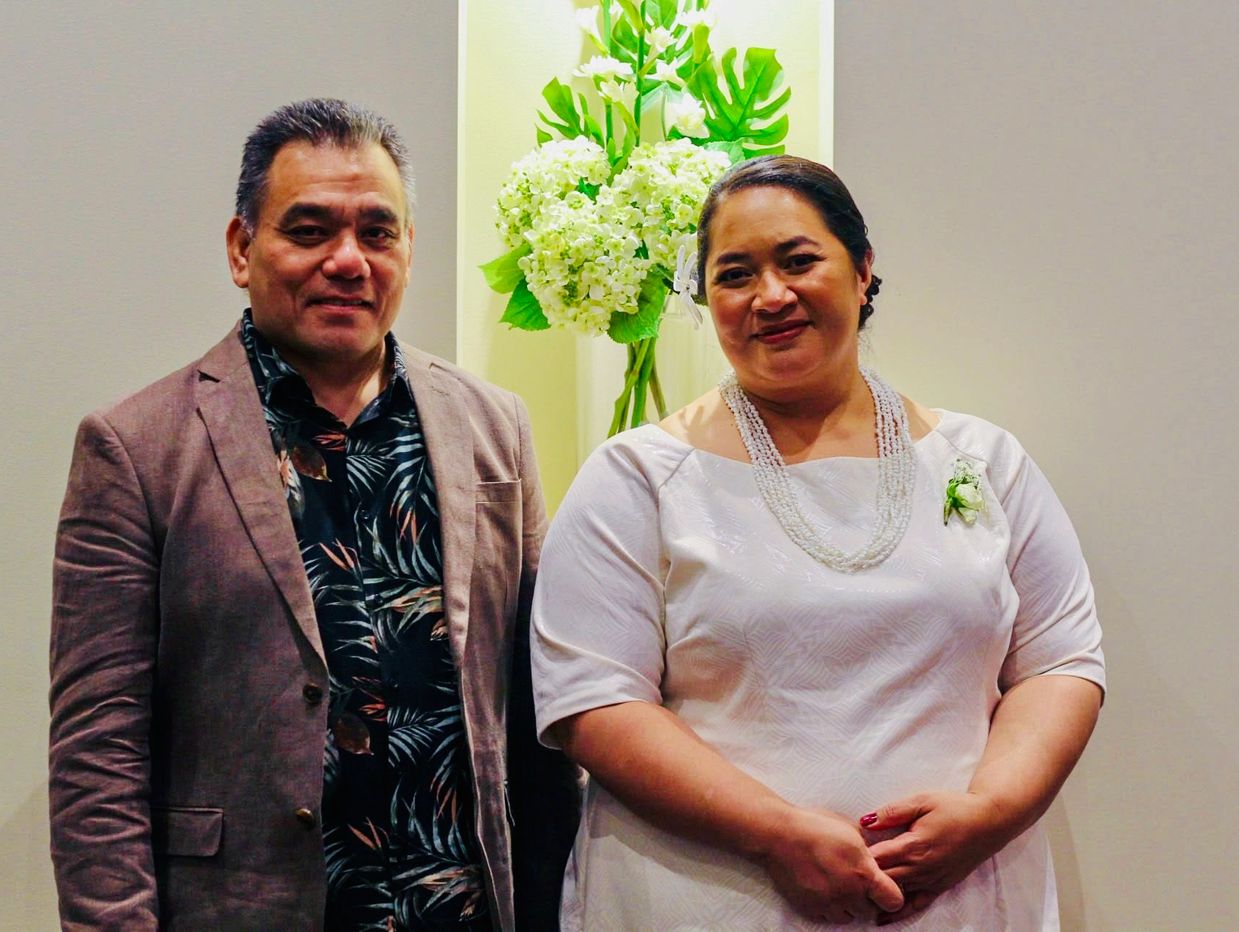 Couple posing with floral arrangement behind them.