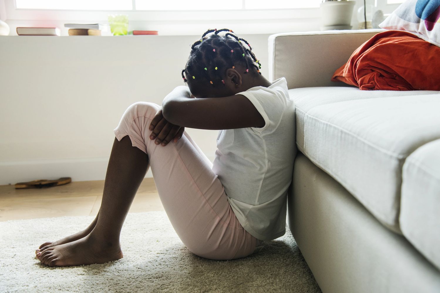 Girl sitting on floor in front of couch with head in crossed arms on her knees.