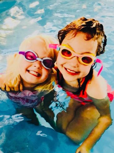 Two kids smiling in a pool with goggles.