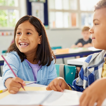 Two children smiling and working together in a bright classroom.