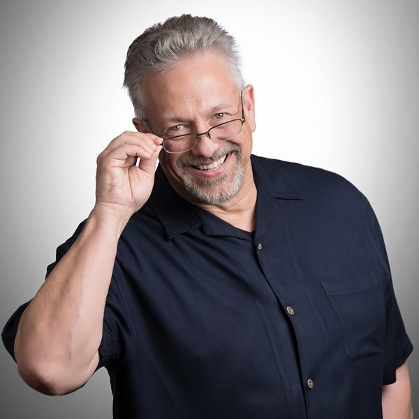 Smiling man adjusting his glasses, wearing a dark shirt.