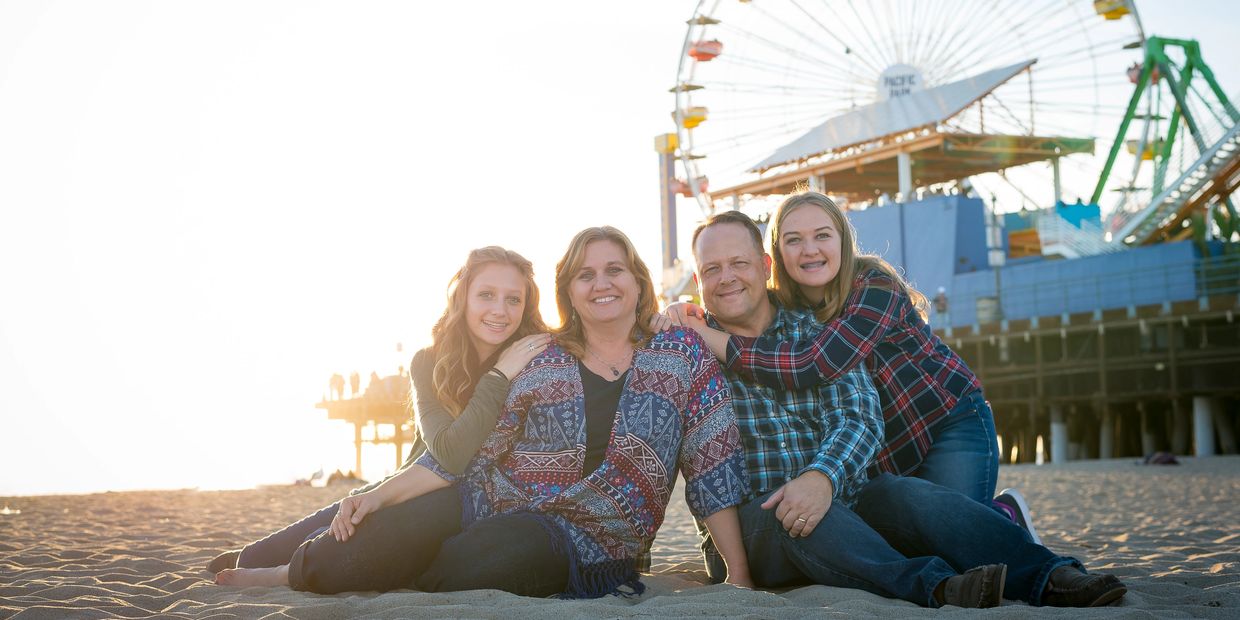 Family of four sitting on the beach with a ferris wheel in the background.