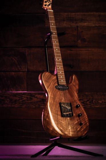 Electric guitar with a wooden finish on a stand against a dark wooden background.
