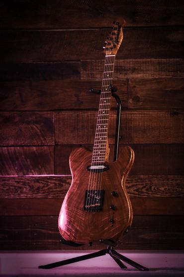 A polished wooden electric guitar on a stand against a wooden wall.