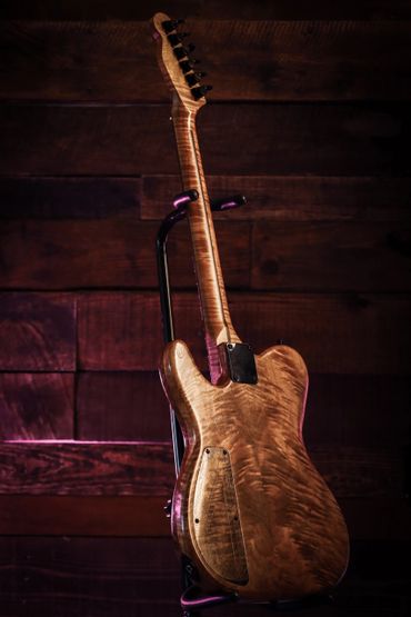 Back view of a wooden electric guitar on a stand with warm lighting.