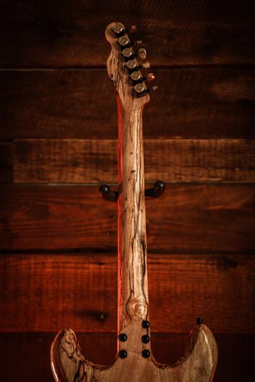 Back view of a wooden electric guitar neck and headstock against a wooden background.