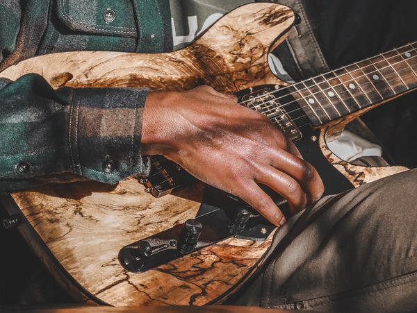 A person playing a wooden electric guitar while wearing a plaid shirt.