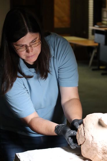 Saint Ignace Museum worker piecing together an idol head to see if it fits
