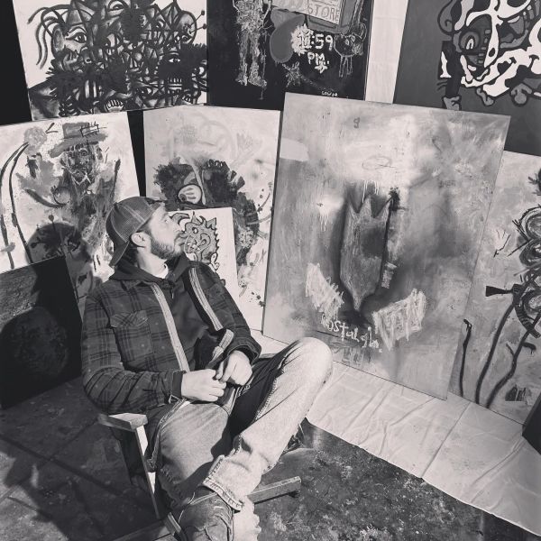 Man sitting near abstract paintings in a studio.