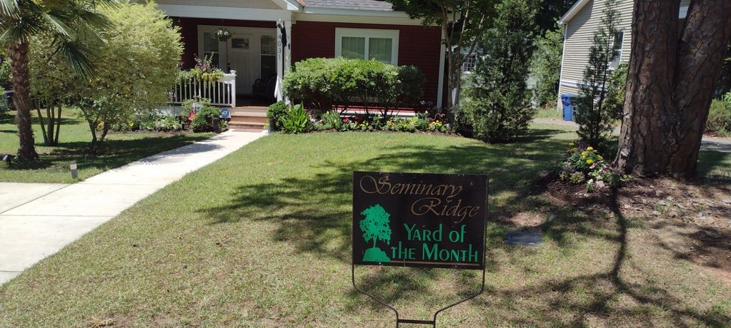 Front yard with a sign reading 'Yard of the Month' in front of a red house.