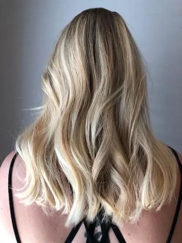 Back view of a woman with wavy blonde hair and dark roots.