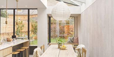 Bright dining area with skylights and a natural wood table, connected to an outdoor garden.