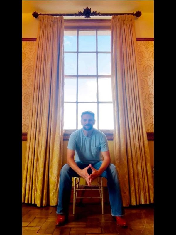 Man sitting on a chair in front of a large window with curtains.