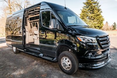 Black luxury Mercedes-Benz van with open sliding door revealing plush interior.