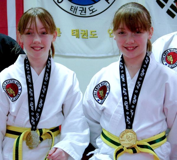 Two young girls in white TKD uniforms, holding gold and silver medals from the Pan Am Games
