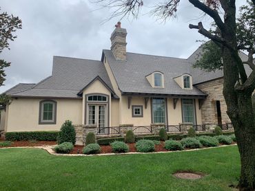 Elegant stone house with a manicured garden and cloudy sky.