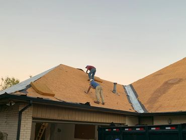 Two workers installing plywood on a house roof during sunset.
