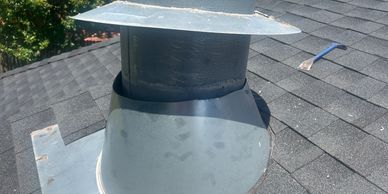 Close-up of a chimney pipe flashing on a shingled roof with a pry bar nearby.