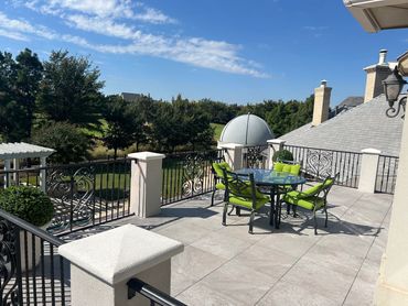 Sunny balcony with green cushioned chairs and a clear blue sky.