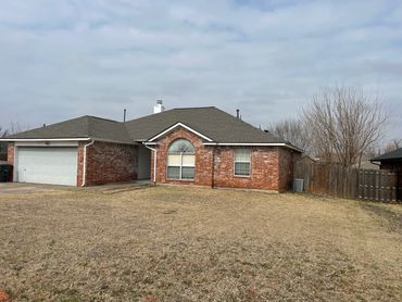 Single-story brick house with a garage and dry lawn under a cloudy sky.