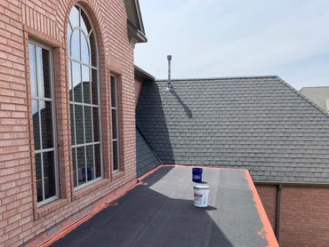 New roofing underlayment installed on a flat section of a brick house roof.