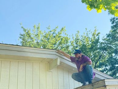 Man crouching on a roof edge inspecting the gutter on a sunny day.