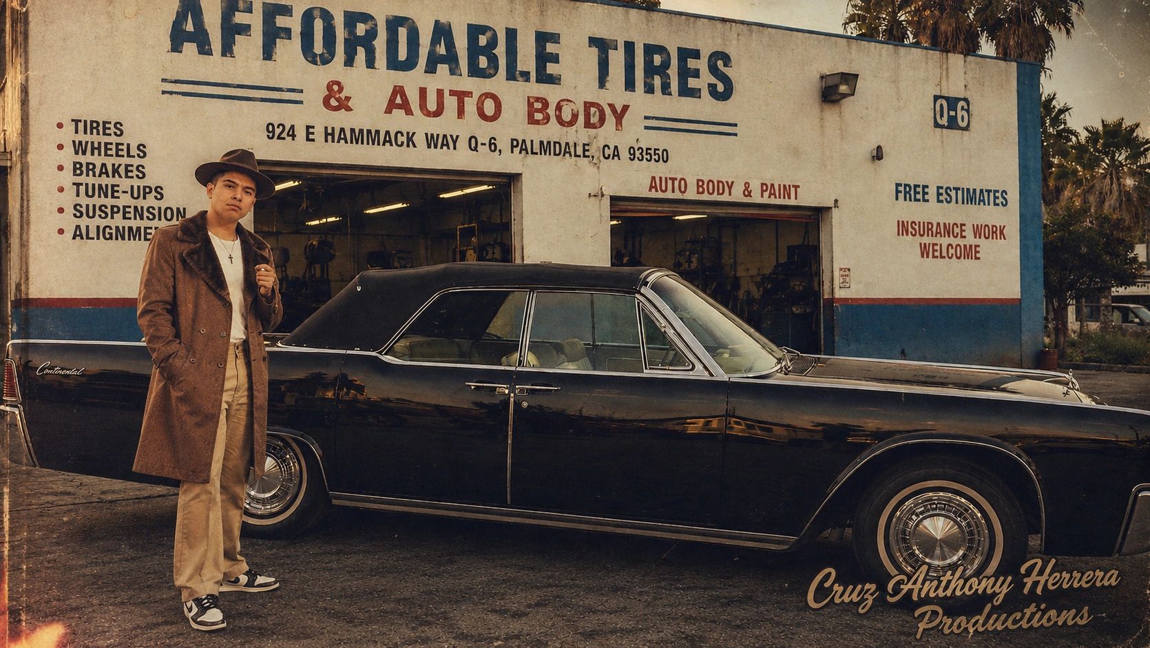 Man standing by a classic car in front of an auto repair shop.