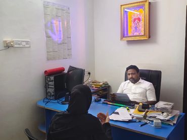 Office meeting between a man and a woman in traditional attire at a cluttered desk.