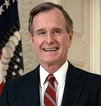 Portrait of a smiling elderly man in a suit with a U.S. flag in the background.