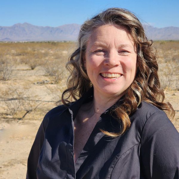 Smiling woman with curly hair in a desert landscape.