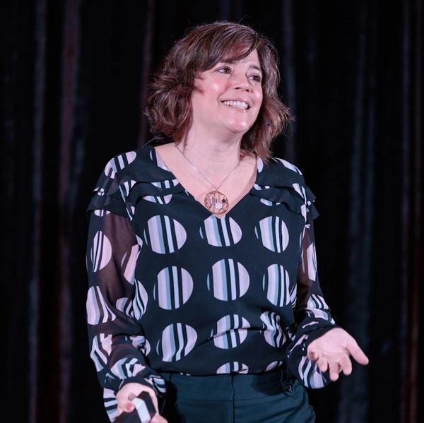Woman smiling and speaking on stage with a microphone in hand.