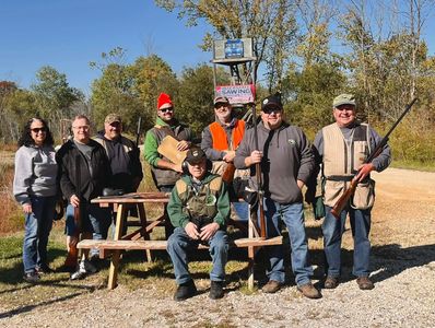 Group of hunters posing with rifles outdoors on a sunny day.