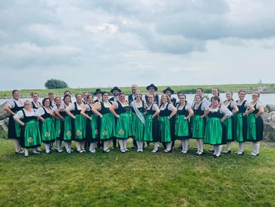 Group of women in traditional green dresses posing outdoors by water.