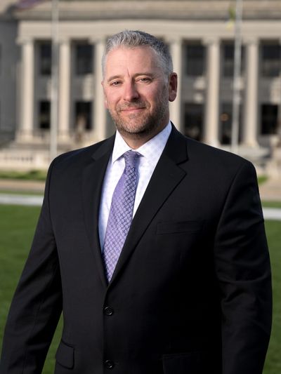 Man in a suit standing outside a formal building with columns.