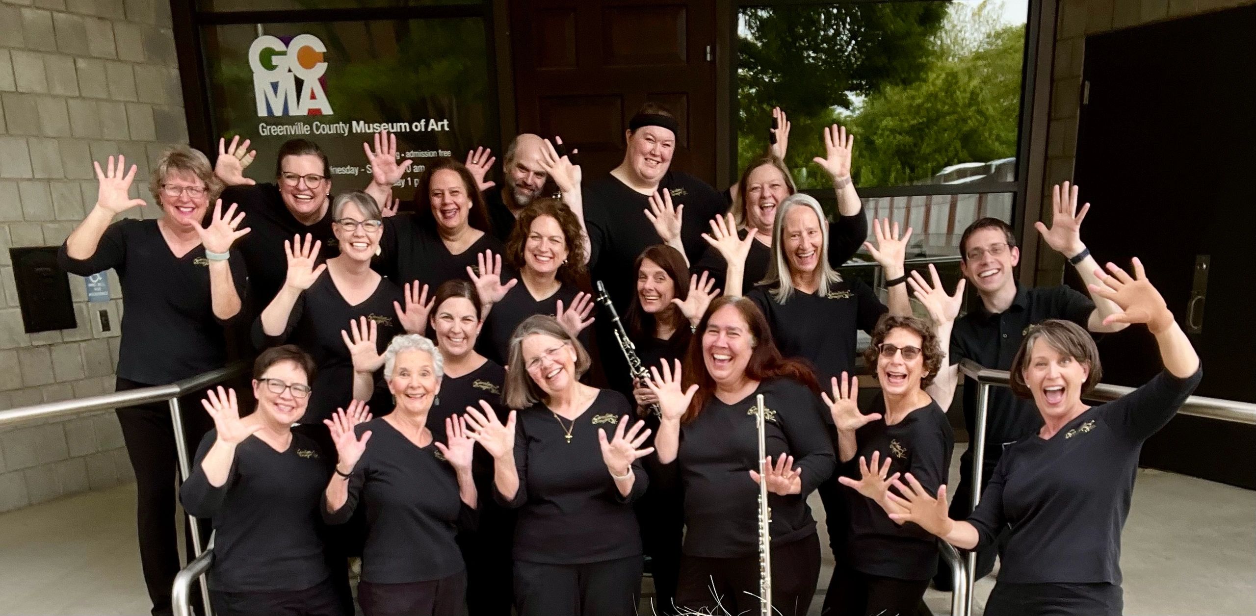 A joyful group of people waving in front of Greenville County Museum of Art.