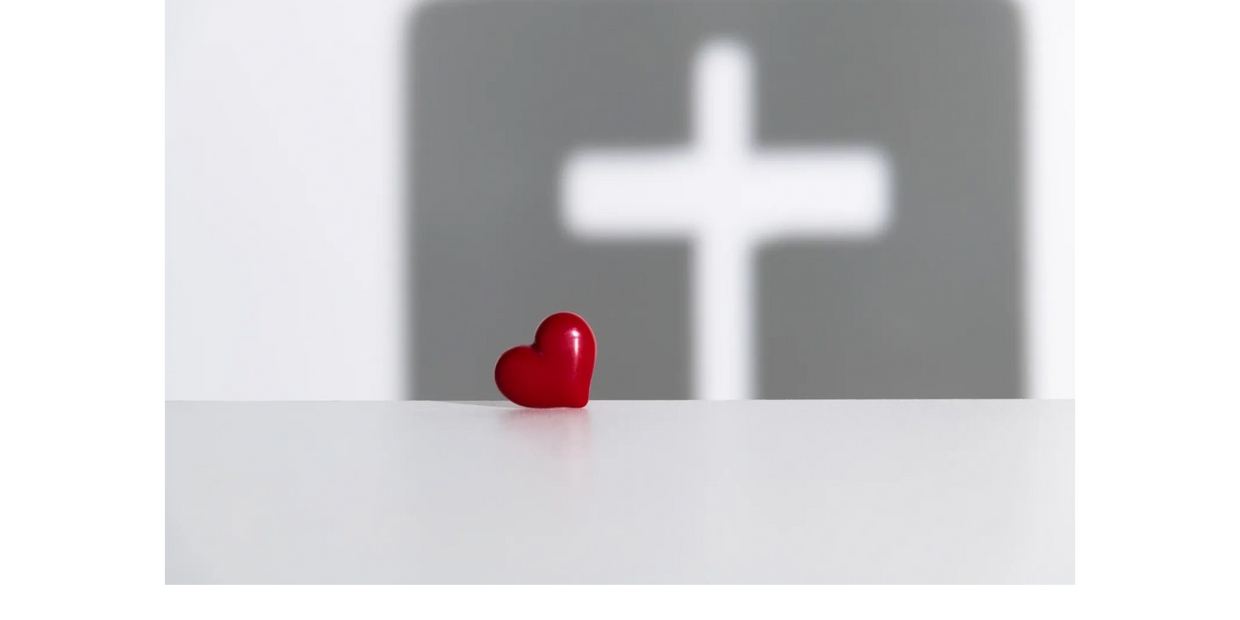 A small red heart with a blurred cross in the background.