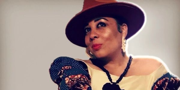 Woman wearing a red hat and patterned dress smiles confidently.