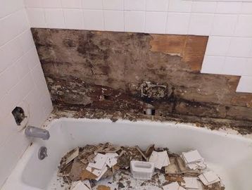 Bathtub area with removed tiles and damaged wall.