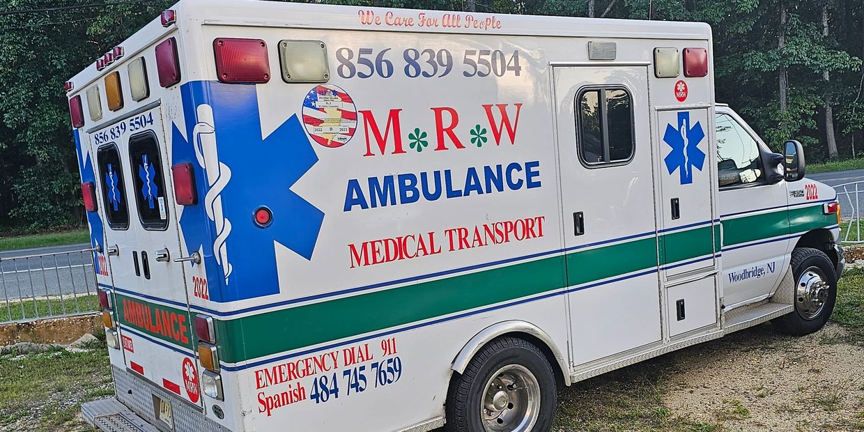 M R W ambulance parked on grass beside a road with trees in the background.