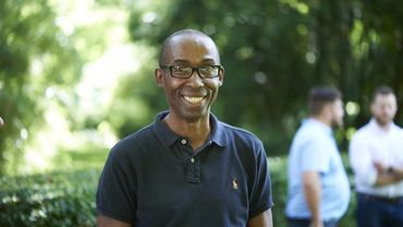 Smiling man in glasses and navy polo shirt outdoors.