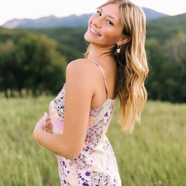 Young woman smiling in a floral dress outdoors with mountains in the background.