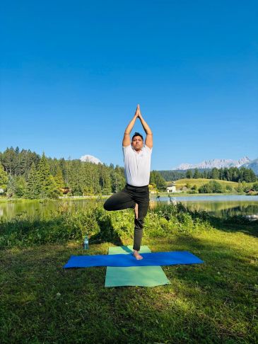 Mand udfører yoga i naturen ved en sø.