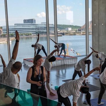 Group practicing yoga indoors with waterfront view through large windows.