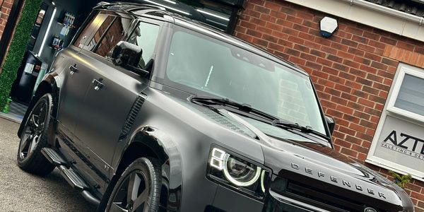 Sleek black Land Rover Defender parked in front of a brick building.