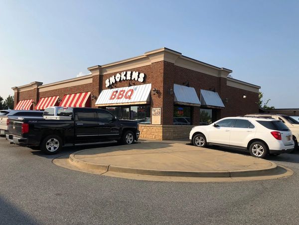 Brick building with striped awnings housing Smokers BBQ restaurant, parked cars outside.