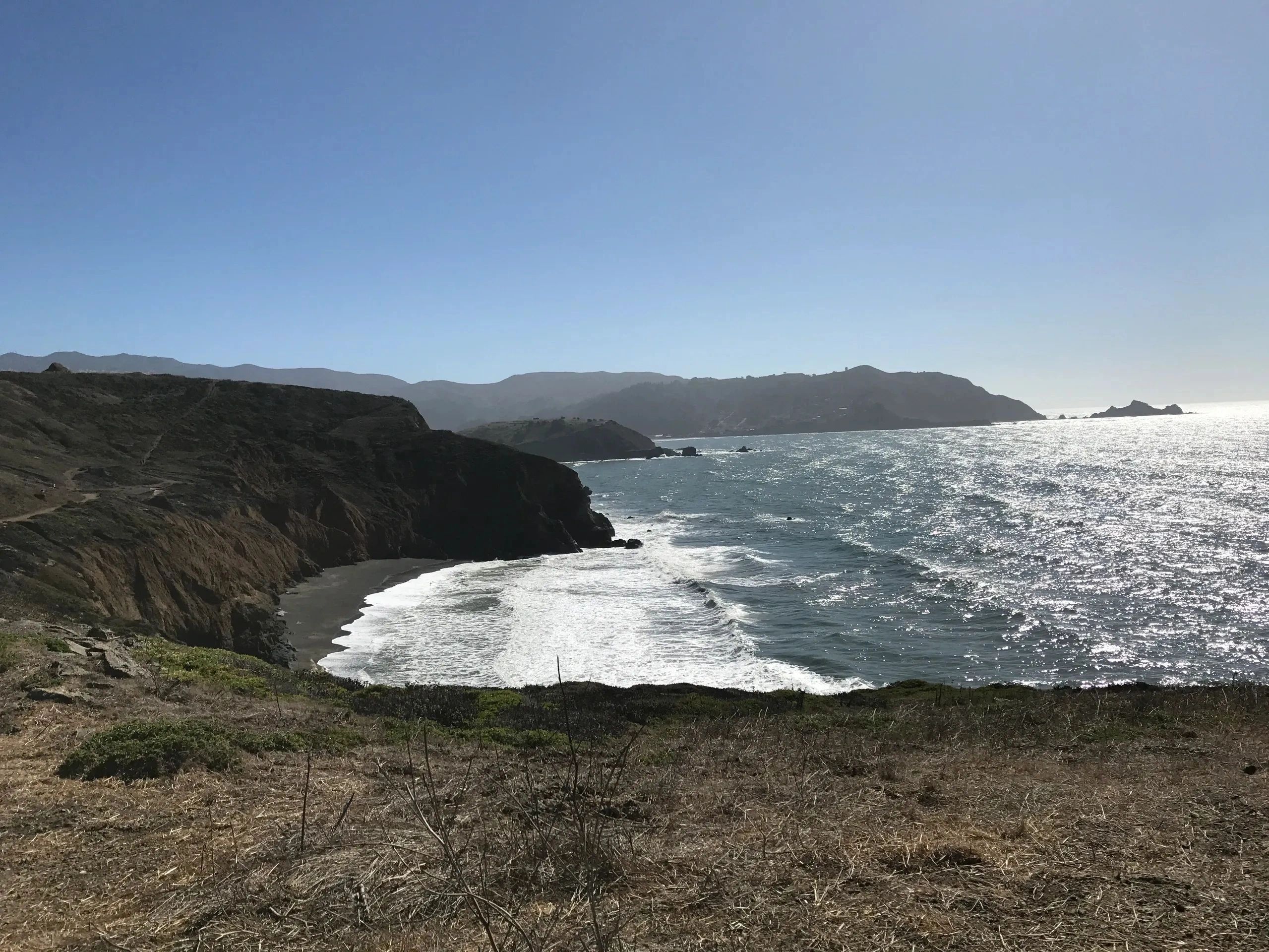 Coastal cliffs overlooking a sunny ocean and beach under a clear blue sky.