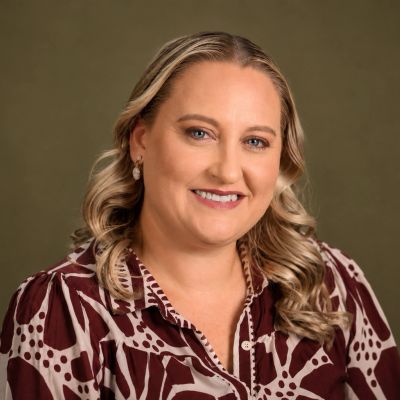 Smiling woman with blonde hair in patterned blouse.