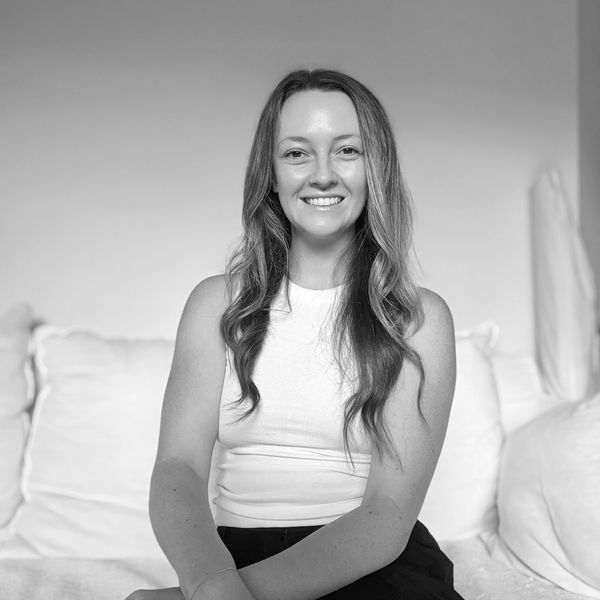 Smiling woman with long hair sitting on a couch in a bright room.