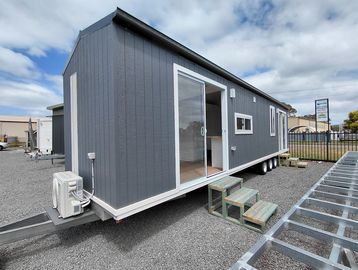 Gray tiny house on wheels with small stairs.