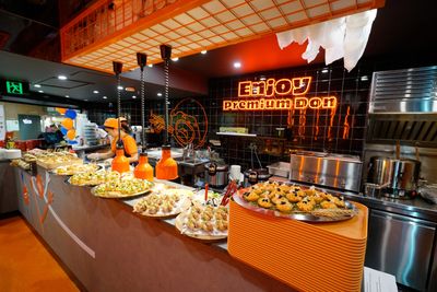 Vibrant food counter with chefs preparing assorted gourmet dishes under bright orange lights.
